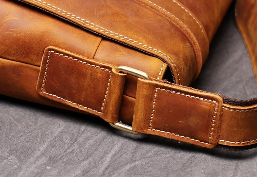 Brown leather messenger bag showing stitching detail and shoulder strap buckle