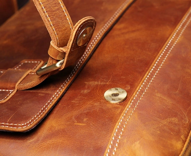 Closeup view of brown leather messenger bag showing magnetic snap button