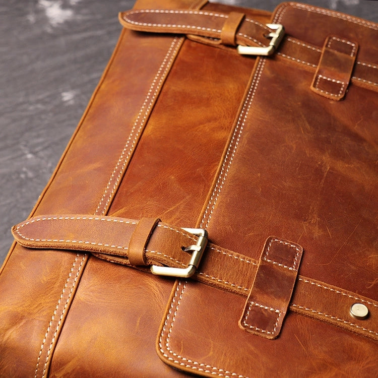 Closeup top view of brown leather messenger bag showing stitching detail and belt straps