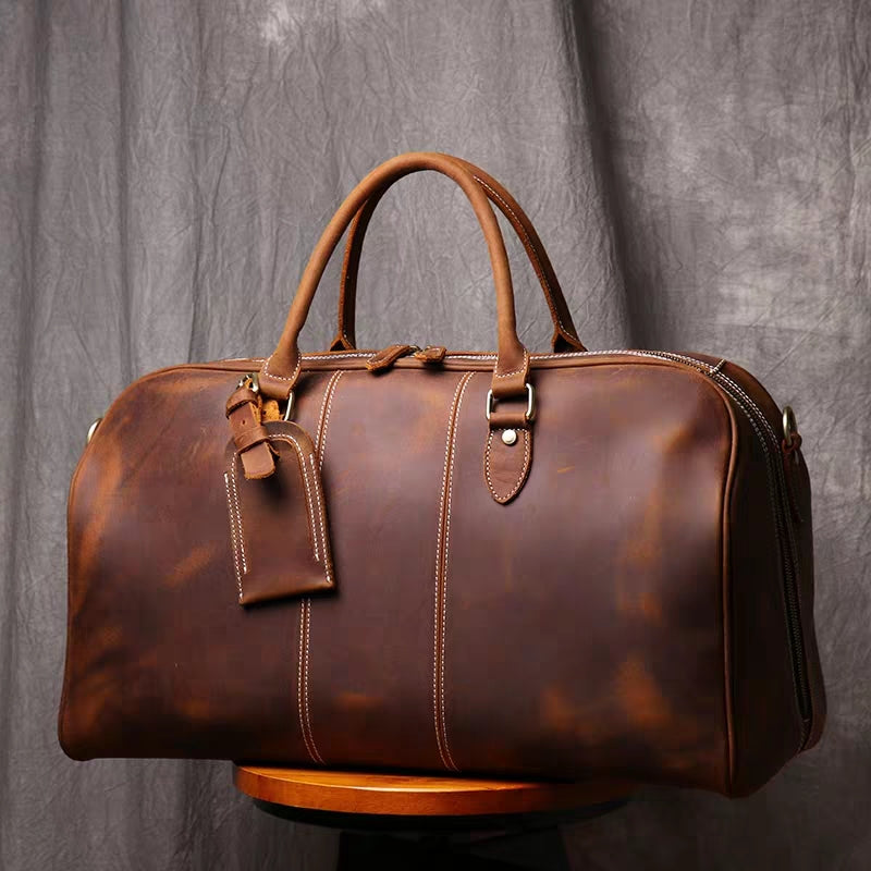 Front view of brown leather duffel bag showing stitching detail and luggage tag holder