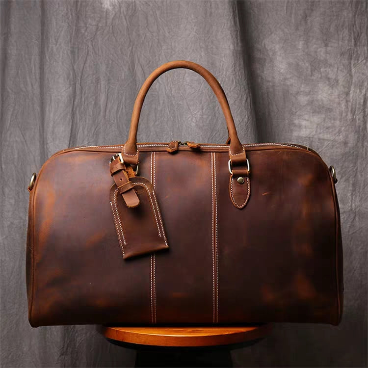 Front view of brown leather duffel bag showing luggage tag and handle 