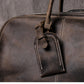 Closeup view of dark coffee color leather duffel bag showing stitching detail and luggage tag