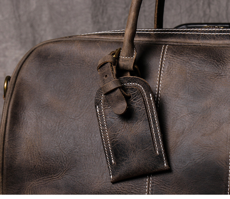 Closeup view of dark coffee color leather duffel bag showing stitching detail and luggage tag