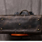 Bottom view of dark coffee color leather duffel bag showing metal studs and stitching detail