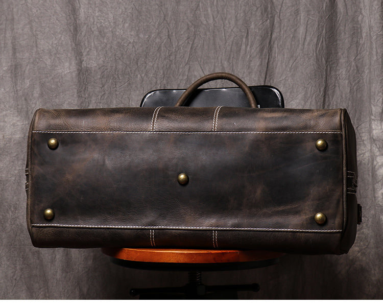 Bottom view of dark coffee color leather duffel bag showing metal studs and stitching detail