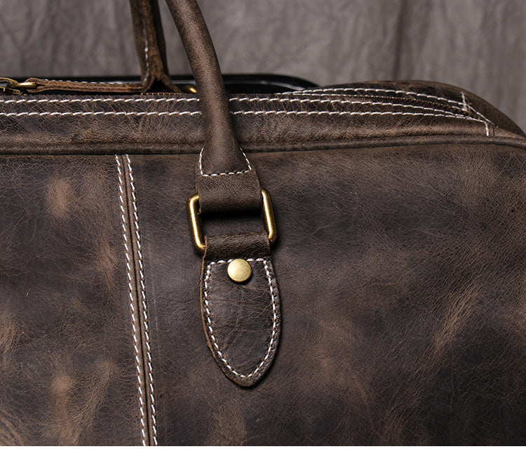 Closeup view of dark coffee color leather duffel bag showing stitching detail handle strap and metal