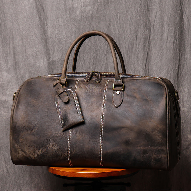 Front view of dark coffee color leather duffel bag showing stitching detail handles and luggage tag strap